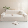 A cream-colored, modern sofa with a light beige rug, featuring a small wooden tray and white floral greenery.