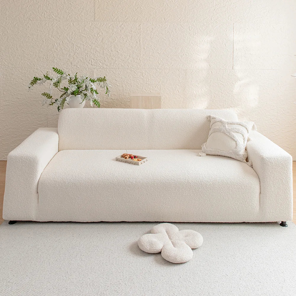 A cream-colored, modern sofa with a light beige rug, featuring a small wooden tray and white floral greenery.