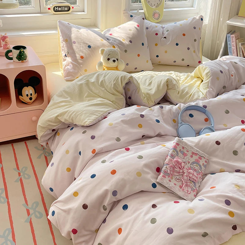 A bed dressed with a white and pink polka dot duvet cover set, pillows, and bedding in a bright room.