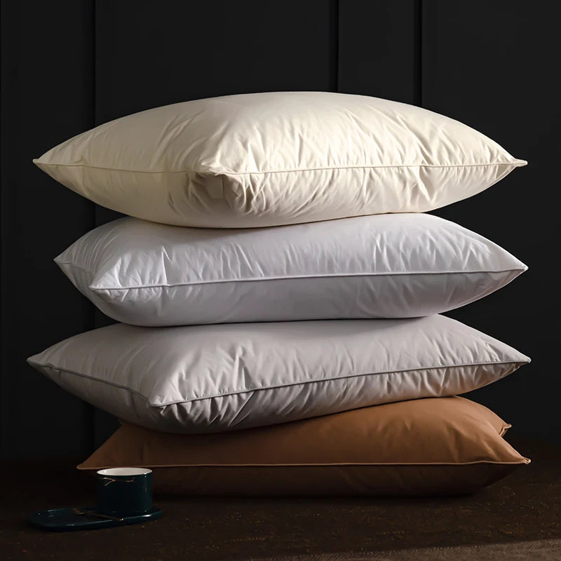 A stack of three natural goose down and feather sleeping pillows in off-white and beige tones.