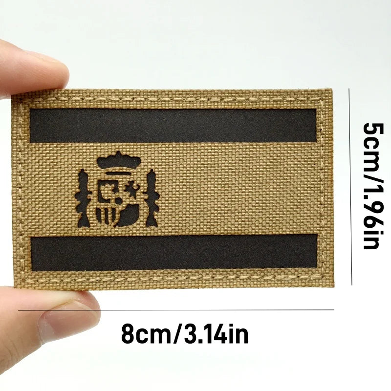 A rectangular tactical patch featuring the Spanish flag emblem on a beige fabric with black stripes.