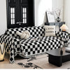 A black and white checkerboard sofa slipcover with a decorative throw and pillows in a modern living room setting.