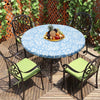 A round blue and white patterned vinyl tablecloth set on a wooden deck with black wrought iron chairs and fruit.