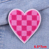 Pink checkered heart shaped iron-on embroidery patch sewn onto a blue denim fabric.