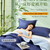 A woman is relaxing on a bed covered with a blue quilted blanket, enjoying a peaceful moment.