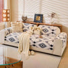 A beige sofa covered in a patterned fleece slipcover with throw pillows and a light-colored rug.