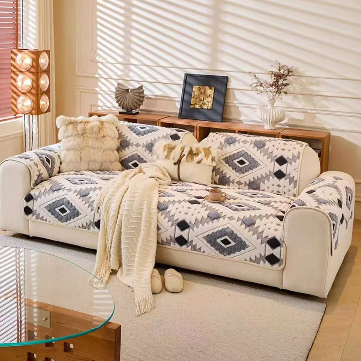 A beige sofa covered in a patterned fleece slipcover with throw pillows and a light-colored rug.
