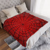 A symmetrical red spider web throw blanket is displayed on a white bed with light gray bedding and a textured rug.