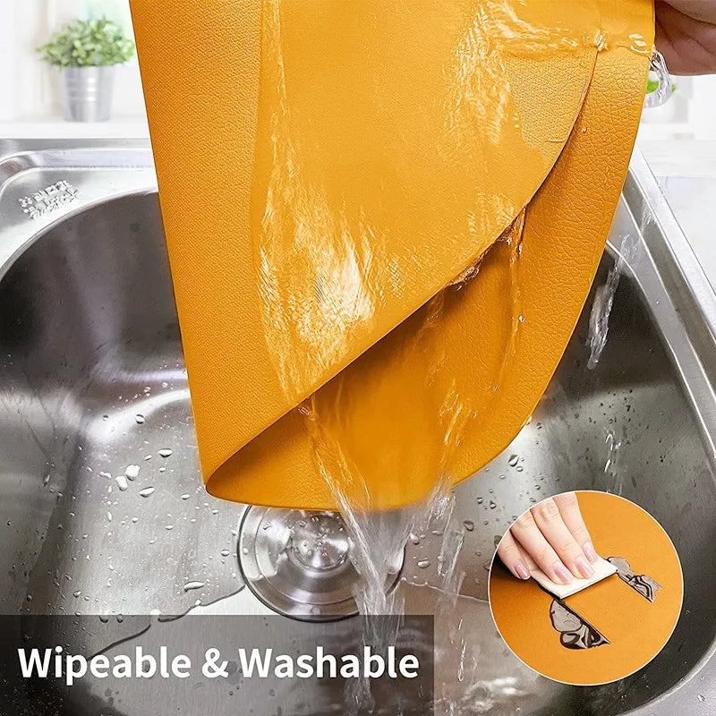 A reusable orange vinyl placemat being washed in a stainless steel sink.