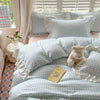 A light blue and white checkered duvet cover set with ruffled pillowcases and a teddy bear on a bed.