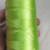 A spool of bright lime green high tenacity polyester sewing thread is held in a hand.