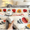 A hand is touching a fluffy, white and gray lamb'swool winter blanket decorated with floral embroidery.