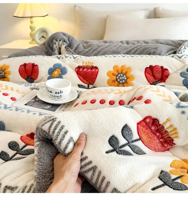 A hand is touching a fluffy, white and gray lamb'swool winter blanket decorated with floral embroidery.