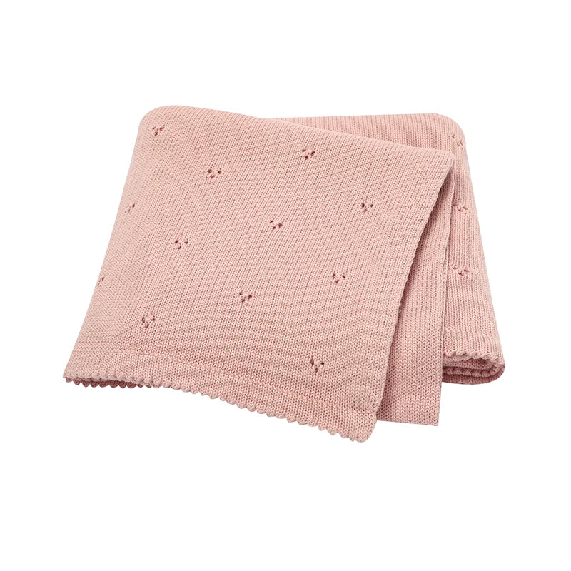 A folded pink cotton knit baby blanket with small eyelet details.