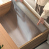 A close-up view of a silicone non-slip drawer liner being placed inside a wooden cabinet or drawer.