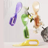 A collection of four modern, twisted-design metal spatulas or lifters in purple, green, gold, and yellow.