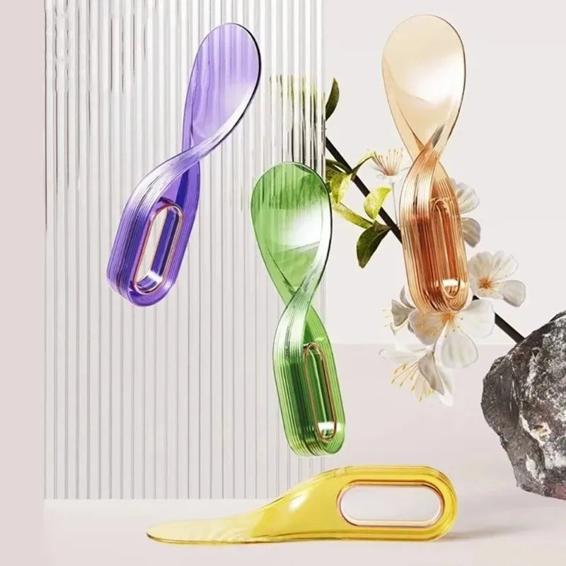A collection of four modern, twisted-design metal spatulas or lifters in purple, green, gold, and yellow.