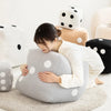 A woman rests her head on a gray plush dice cube cushion surrounded by various soft, polka-dotted cushions.
