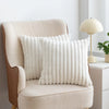 A cream upholstered armchair with a white faux fur decorative throw pillow on it.