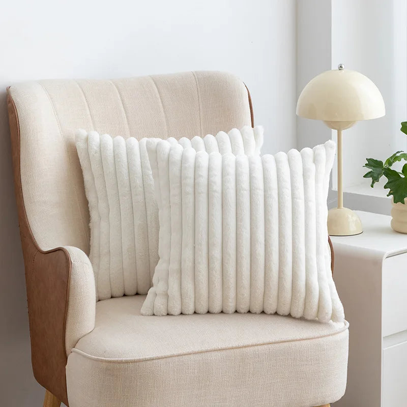 A cream upholstered armchair with a white faux fur decorative throw pillow on it.