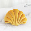 A golden velvet stuffed sofa cushion shaped like a decorative seashell resting on white bedding.