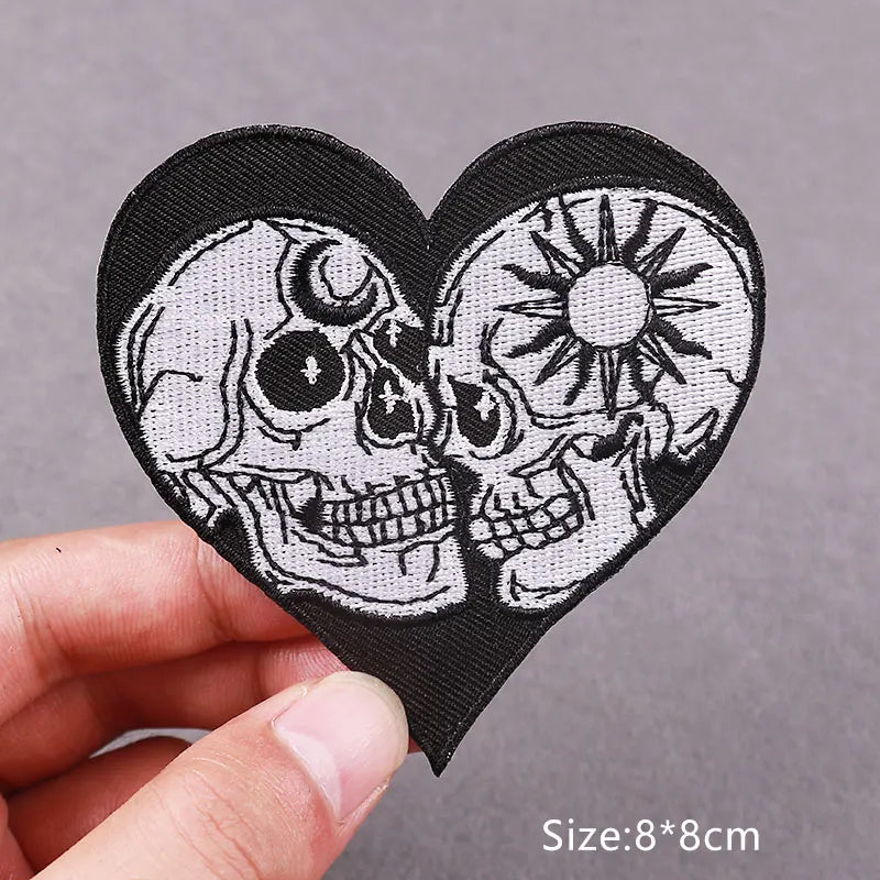 Black heart-shaped embroidered patch featuring two skulls with sun motifs