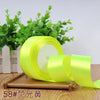 A roll of bright lime green satin ribbon for gift wrapping and DIY crafts, set against a blurred green plant background.