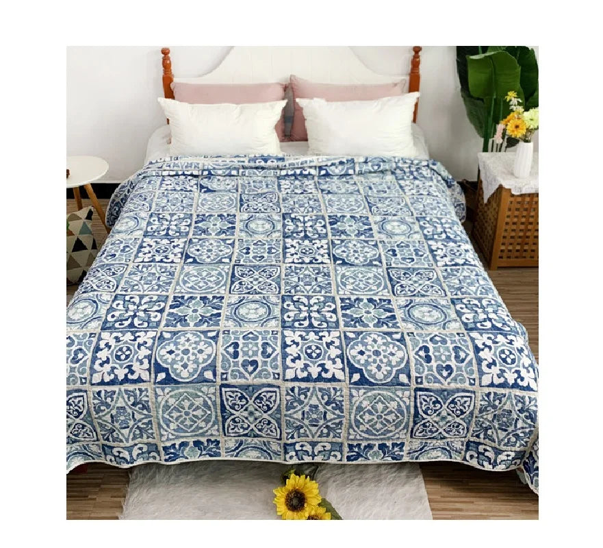 A blue and white embroidered cotton quilted bedspread on a bed with white pillows.