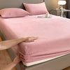 A close-up of pink luxury velvet bedding, including a sheet and pillow, being touched by a hand.