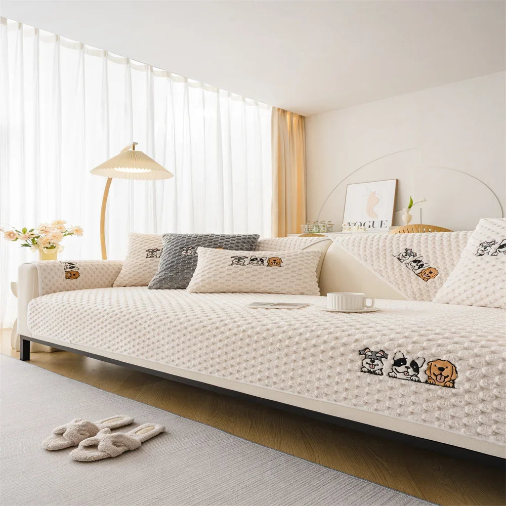 A beige plush sofa cover with a quilted texture is displayed on a bed, next to a modern lamp and sheer curtains.