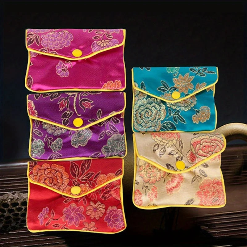 Three silk brocade jewelry pouches in pink, purple, and teal colors with yellow accents.