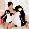 A pair of black and white penguin plush toys sitting on a light-colored sofa.