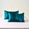 A teal satin pillowcase with an envelope closure resting on a white surface.
