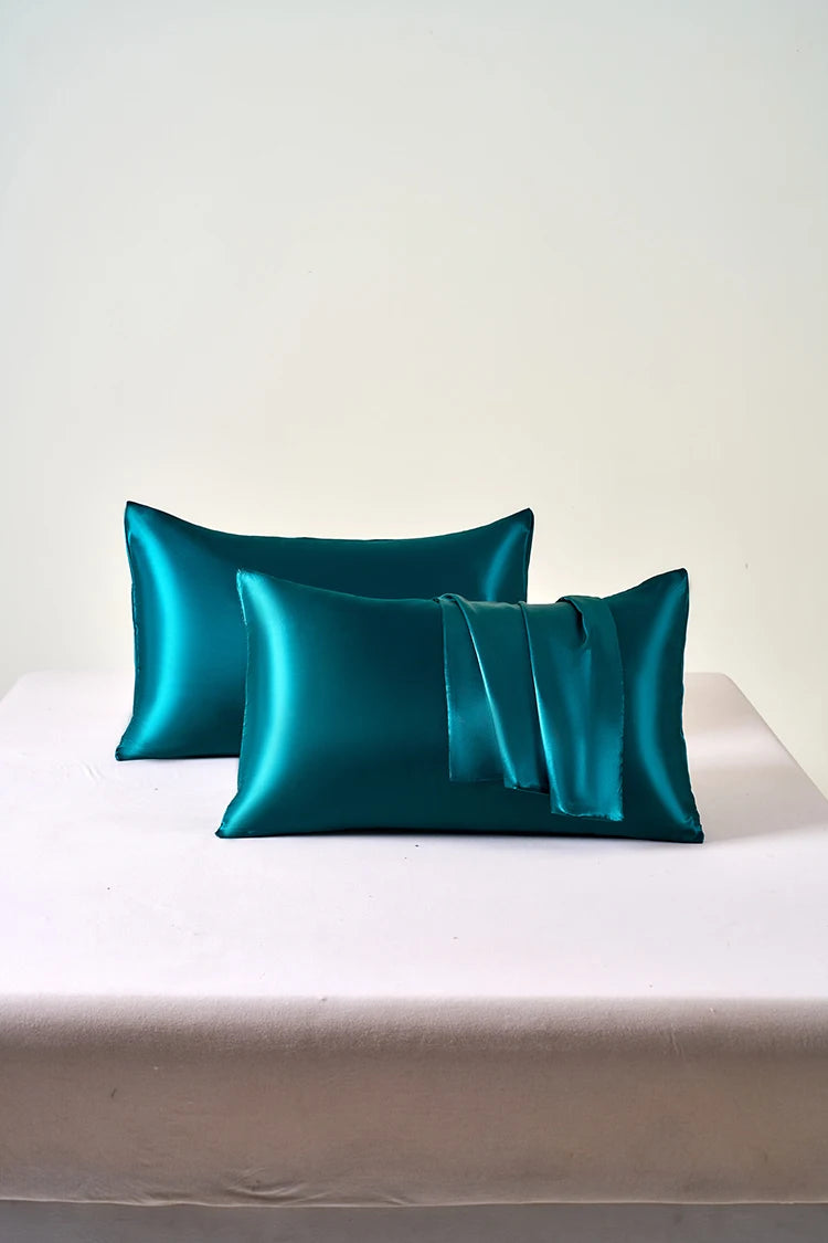 A teal satin pillowcase with an envelope closure resting on a white surface.
