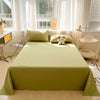 A light green organic cotton bedding set displayed on a bed with white curtains and natural light.