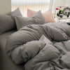 A bed with a gray duvet cover and pillows, featuring pink accent pillows.