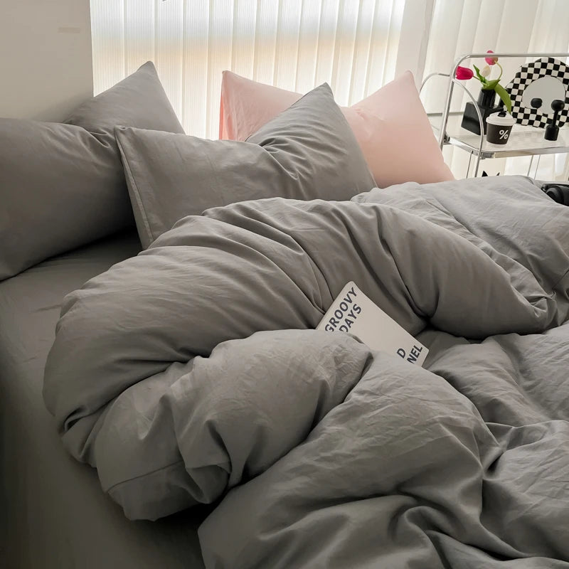 A bed with a gray duvet cover and pillows, featuring pink accent pillows.