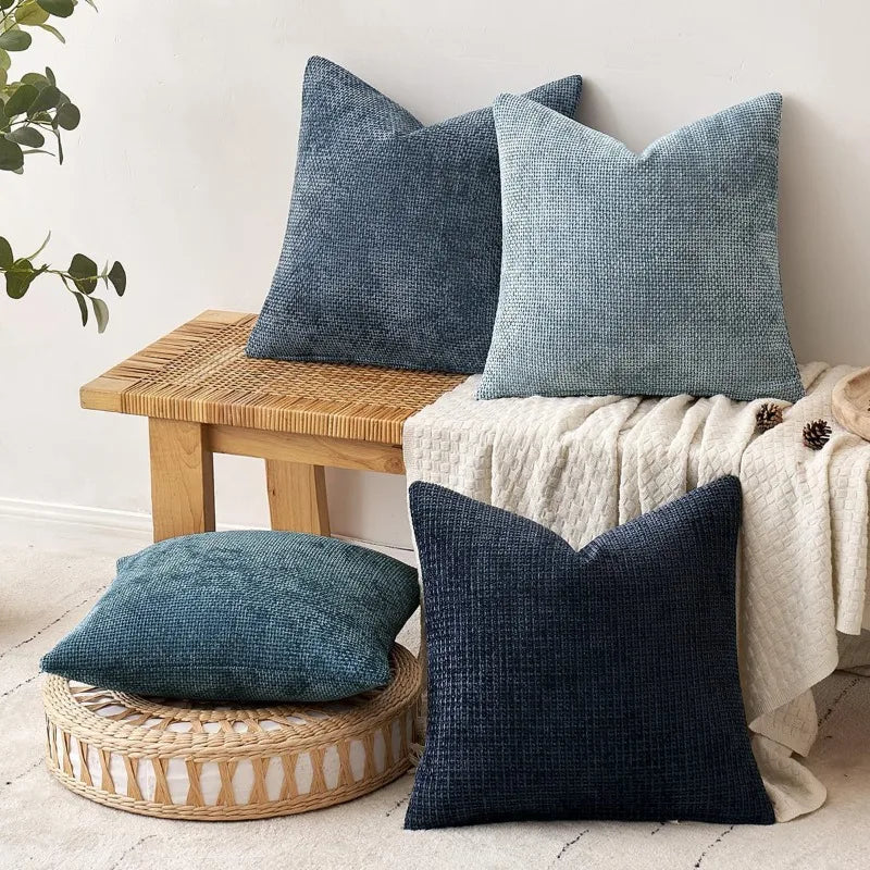 A collection of textured blue and gray chenille pillows displayed on a wooden surface.