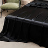 Black satin flat bed sheet draped on a bed, next to a light green upholstered chair.