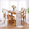 A wooden dining table set with a white embroidered floral lace table runner and sheer white fabric on the chairs.