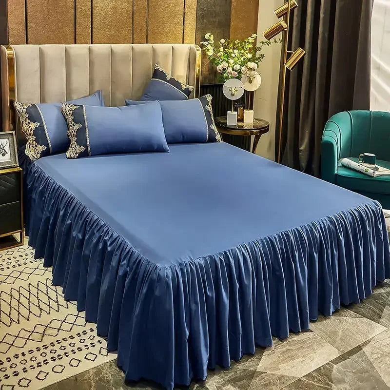 A luxurious bed set featuring a royal blue duvet and skirt with lace edging, set against a neutral backdrop.