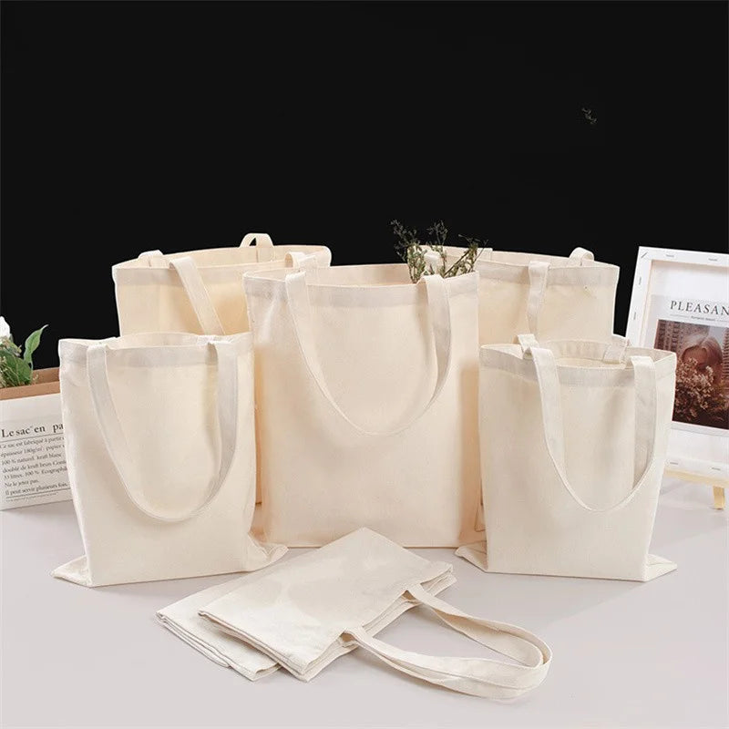 Several natural canvas tote bags in beige and off-white are displayed on a white surface.