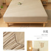 A beige fitted sheet set and pillow displayed on a wooden bed frame with natural light.