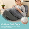 A woman is using a soft, gray ergonomic J-shaped maternity pillow while sitting down.