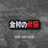 Black embroidered badge with Japanese text 全村の希望 (Zen-son no Kibou) on a dark gray textured background