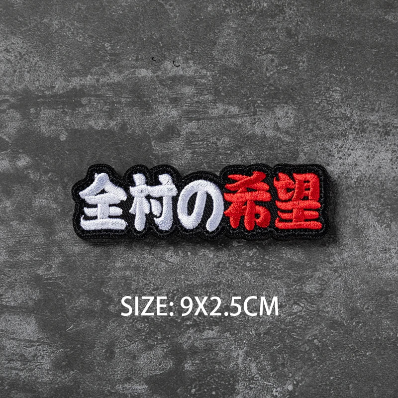 Black embroidered badge with Japanese text 全村の希望 (Zen-son no Kibou) on a dark gray textured background