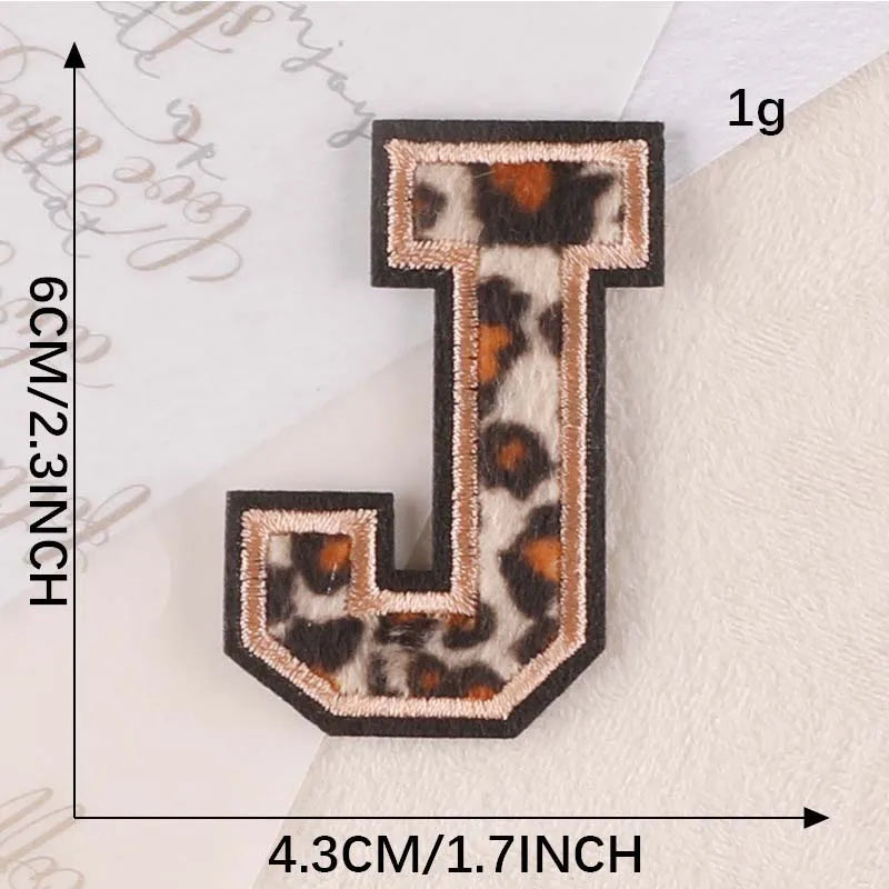 A leopard print letter J iron-on patch with a dark brown border and gold lettering.