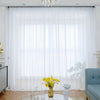 White semi-sheer tulle curtains with a delicate floral texture hanging in a bright room.