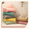 A stack of various colored flannel towels, including pink, teal, gray, yellow, and beige, displayed on a white surface.