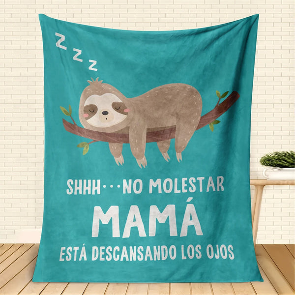A teal throw blanket featuring a sloth illustration and Spanish text that reads Shhh no molestar mamá está descansando los oj